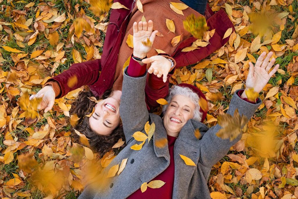 2 woman surrounded by leaves laying on the ground